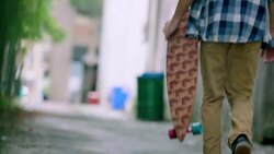Young man walks through downtown alley carrying custom skateboard Stock Footage