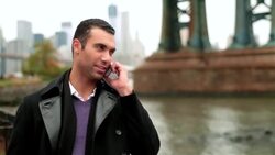 Man laughs, talks on smartphone in front of Manhattan Bridge on the East River Stock Footage