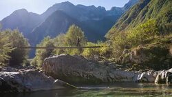 Young woman crossing a suspension bridge over mountain stream Stock Footage