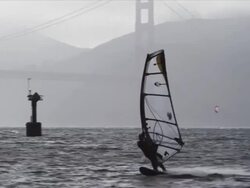 Windsurfer on San Francisco Bay speeds towards camera then turns sharply, Golden Gate Bridge in background Stock Footage