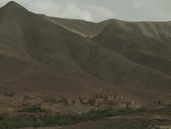 Vast, steep North African mountains lead down to an old style village or settlement. Stock Footage