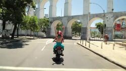 Girl throws hands in the air and cheers as mototaxi drives under Rio's famous Arcos da Lapa Stock Footage