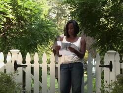 Black woman opening mail next to garden gate, worried husband approaching Stock Footage
