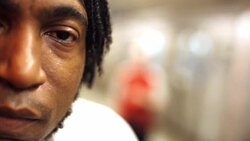 Street artist stares at camera on New York City subway platform as train leaves station Stock Footage