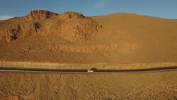 High angle drone footage of car moving on road by rocky mountain, High Atlas, Morocco Stock Footage