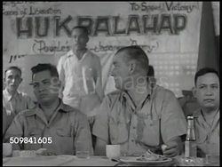 1945: PHILIPPINE HUKBALAHAP: WS Hukbalahap meeting, banner. MS American & Philippine man sitting at table, man giving speech w/ hand gestures BG. CU Banner 'Hukbalahap.' MS Philippine men listening. Instructional Video