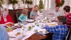 Family pass plates around table for Christmas dinner, mother scoops mashed potatoes onto young daughter's plate (dolly-shot) Stock Footage