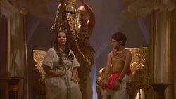 A priest wearing a leopard skin robe places a gold crown on a woman sitting next to a boy in a throne room. Stock Footage