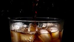 Pouring cola soda into glass of ice with splashes at slow motion on black background Stock Footage