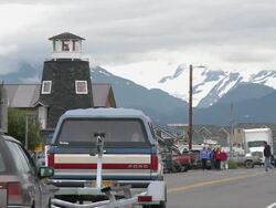 "Homer Spit Road with lighthouse of The Salty Dawg Saloon to left, cars passing both directions, houses visible in background, snow capped mountains of Kachemak Bay State Park and Wilderness Park visible, Home, Kenai Peninsula, Alaska." Stock Footage
