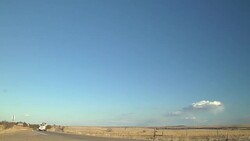 Semi truck carries a backhoe on a trailer and drives down a rural highway and passes a farm tractor discing a field. Stock Footage