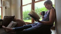 Senior woman relaxing and reading book drinking coffee in living room Stock Footage