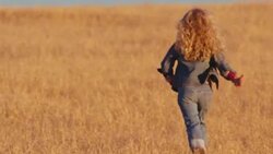 Little girl with blonde hair runs away from camera in a field of golden prairie grass. Stock Footage