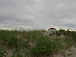 Wide shot of the Coast Guard house on the National Seashore in Cape Cod with a sand dune and dune grass in the foreground. Stock Footage