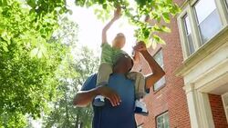 MS LA Smiling boy riding on fathers shoulders reaching up towards leaves on tree during walk in park Stock Footage