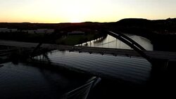 The Sun Sets behind the 360 Bridge or Pennybacker Bridge and Boats go under the bridge as the Silhouette glow of the sun dips behind the Texas Hills Stock Footage