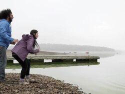 WS side view two young people skimming stones on lake Stock Footage