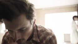 Young man broods on motel bed as young woman paces intensely in background Stock Footage