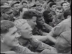 B/W 1967 close up PAN PROFILE crowd of soldiers sitting on ground watching USO show / Vietnam War Stock Footage