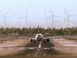 WS passenger jet takeoff from runway and lifting into sky above spinning turbines of wind farm / Palm Springs, California, USA Stock Footage