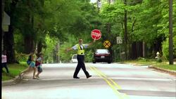 A crossing guard holds stop sign as children cross a street on their way to school. Stock Footage