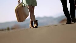 Young couple hold hands walking up a lonely desert road Stock Footage