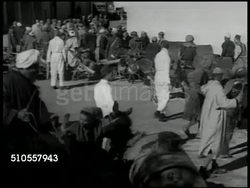 1951: CASABLANCA, MOROCCO: WS Modern apartment building, cattle in dirt FG. SLUMS: People washing clothes in square, crowd of 'water peddlers' crowding into bathhouse. Man adding disenfectant into water barrels. 'Peddlers' being deloused w/ DDT spray. Instructional Video