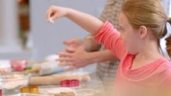 Happy young girl sprinkles flour on flattened cookie dough in kitchen Stock Footage
