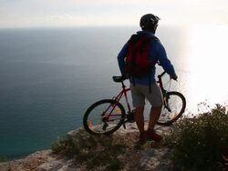 Mountain biker pauses on cliff above sea, sunset Stock Footage