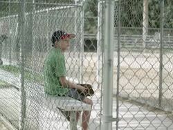 Slow motion push of boy sitting in dugout behind chain link fence. Stock Footage
