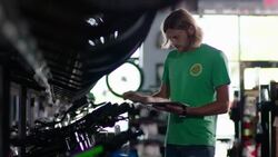 Bike shop employee hangs price tags on new bicycles and manages prices on tablet computer Stock Footage