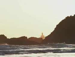 WS SLO MO View of lighthouse is silhouette against rocky Pacific coast as waves pound sand at sunset / Astoria, Oregon, United States  Stock Footage