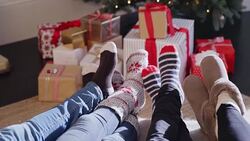 Friends relaxing in socks with feet up on ottoman facing Christmas tree Stock Footage