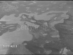 1952: SHALLOW-WATER DRILLING: Brief AERIAL Two oil rigs at edge of marshland off waterway, first w/ no outbuildings, second w/ several & tall derrick.       Marshes, wetlands, Gulf Coast, Louisiana, bayous, petroleum production, Global Warming Instructional Video