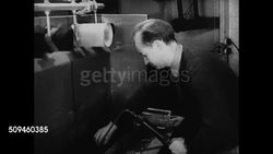 1938: DR. HERTY KEEPS WORKING: Door sign:'Rayon Dep't' WS Dr. Herty at desk watching assistants. VS Male assistant working w/ rayon fibers, pulling fiber over rotating roller. Dr. Herty w/ sample chart of rayon rope. TU Pine tree tops moving in wind. Instructional Video