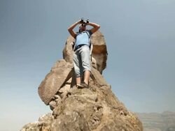 Young man standing on a cliff of mountain and looking through a binocular  Stock Footage
