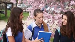 Three teen girls in school uniform walk thru parkiing lot and share information Stock Footage