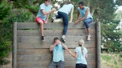 Teammates helping woman over wall at boot camp obstacle course Stock Footage