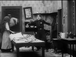 B/W 1917 large man (Eric Campbell) chasing policeman Charlie Chaplin around room Stock Footage