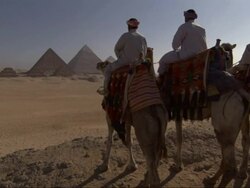 Wide Shot, crane - Three men on camels stand on a hill near the Great Pyramids in Egypt Stock Footage