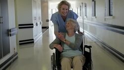 Nurse pushing patient in wheelchair down hospital corridor Stock Footage