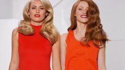 Two women jumping simultaneously creating movement and volume in wavy hair whilst wearing bold colours Stock Footage