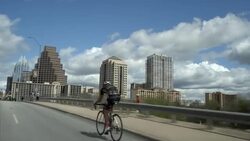 Athletic cyclist on bike pedals fast across bridge into downtown Austin, Texas Stock Footage