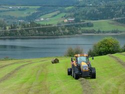 Fagernes Norway farming tractor riding and rolling wheat for cattle with beautiful setting of water and mountains Stock Footage