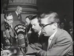 A line of reporters talk into The Voice of America microphones. News Clip