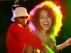 Slow motion handheld man wearing tracksuit and hat singing into microphone, gesturing, young woman wearing sequined minidress dancing beside him Stock Footage