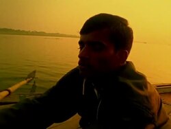 Slow motion medium shot pan Indian man rowing boat on Ganges River at sunset / Varanasi, India Stock Footage