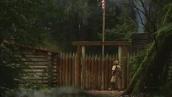 A man in pioneer clothing enters a rustic gate between log cabins. Stock Footage