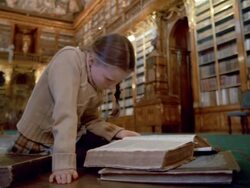 Low angle medium shot girl reading book on floor in Philosophical Hall library at Strahov Monastery / Prague Stock Footage