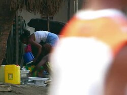 MS Shot of women washing pans outside house and people walking on road / Conakry, Guinea Stock Footage